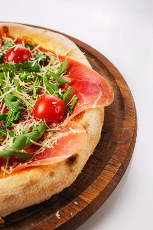 Top view of hot pizza on a wooden stand. Prosciutto, tomatoes, Dutch cheese.の写真素材