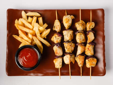 Chicken Skewers. Pieces of tender chicken fillet, grilled with sweet onion rings, and garnished with french fries and tender tomato sauce.の写真素材