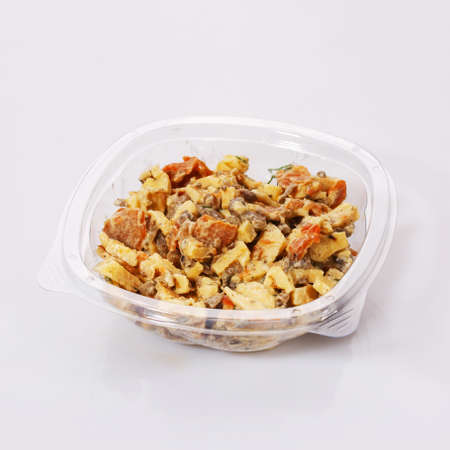 Salad of carrots, meat, cheese and sauce in a transparent plastic bowl on a white background.の写真素材