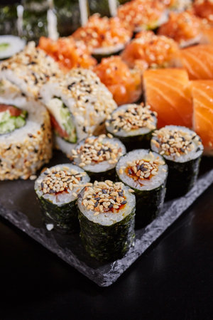 Close up of maki sushi sprinkled with sesame seeds on a stone plate on a dark background.の写真素材