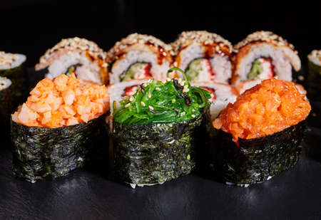 Sushi rolls with seaweed, shrimp, salmon and sprinkled with sesame seeds on a black board on the background of other sushi rolls. Close up of three pieces of sushi with different fillings.の写真素材