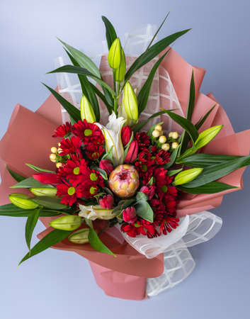 Top view of a bouquet of flowers packed in a white and pink wrapper stands on a blue background.の写真素材