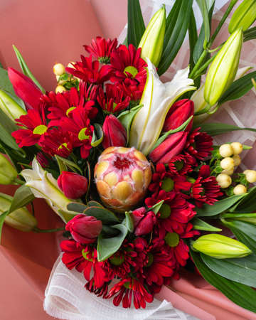 Close up top view of bouquet of bright flowers in red and green colors wrapped in paper.の写真素材