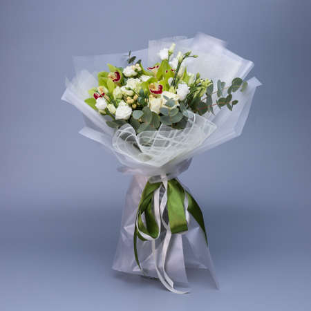 Flower bouquet in light green color, which is wrapped in light floral paper stands on a blue background.の写真素材