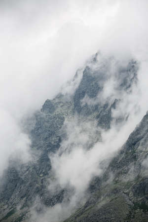 mystical photo of rough rocky mountains surrounded by a white blanket of cloudsの写真素材