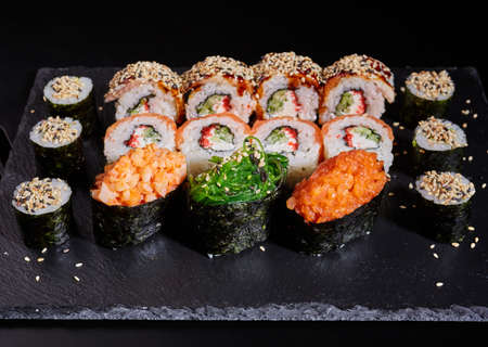 Close up of a set of sushi rolls on a black stone board on a dark table.の写真素材