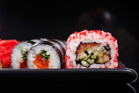 Rice Japanese rolls of Uramaki and Maki with salmon, cucumber, and red caviar on a black plate.の写真素材