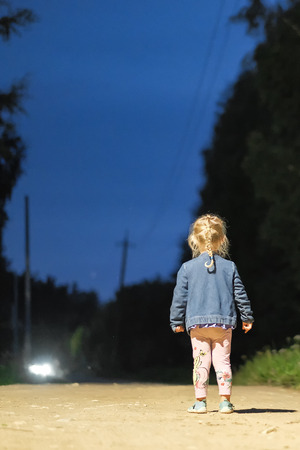 little defenseless girl standing alone in the middle of the road at nightの写真素材