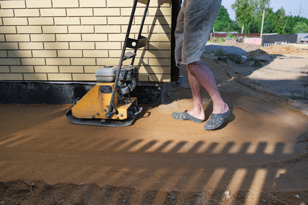 Builder ramming sand around the house at the construction site