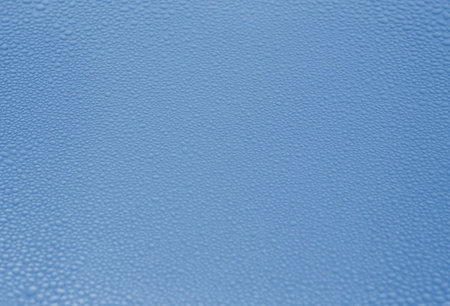 Fine transparent drops of rain water or condensate on a rough blue metal surface