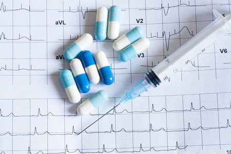 Syringe and tablets on the paper with graph of heart rhythmの写真素材