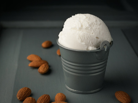 Ice cream ball in decorative bucket on wooden background with almond nuts.の写真素材