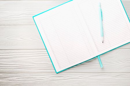 Top view green cover notepad with pencil on white wooden table.