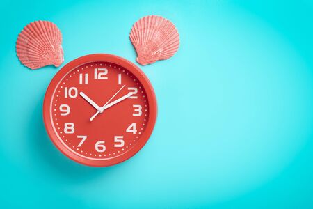 Red clock with shells resembling the head of an animal on a green background with copy space.