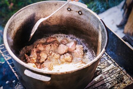 Pieces of beef meat are fried in a cauldron over an open fire.の写真素材