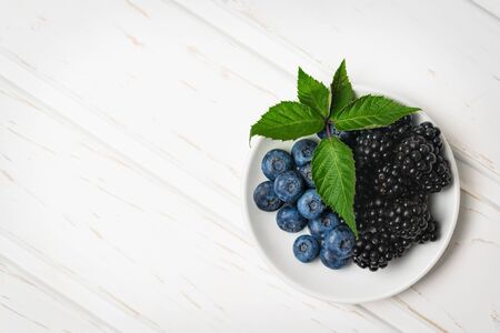 Top view ripe blackberries and blueberries in a white dish on a wooden table with copy space.の写真素材