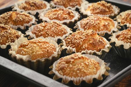 Baked cupcakes with sesame seeds in aluminum molds on a baking sheet.