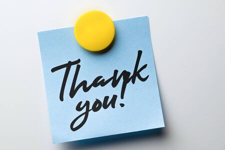 Close-up note with words of thanks written in handwritten font attached with a magnet to a metallic...
