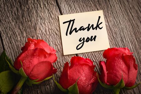 Thank you paper note and red rose buds on wooden background: concept of gratitude.の写真素材