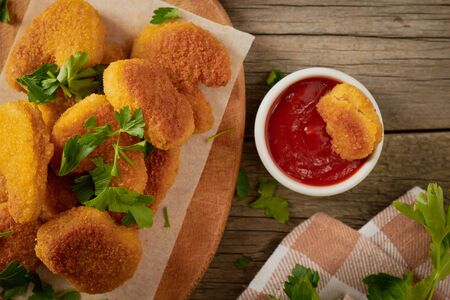 Top view chicken nuggets with parsley leaves on a cutting board and slice nuggets in tomato sauce.の写真素材