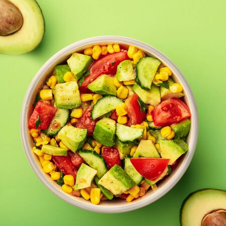 Top view tasty avocado salad with tomatoes, cucumbers in bowl on green background.の写真素材