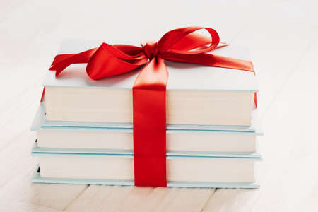Books tied with gift ribbon on white wooden background: concept of donating books.の写真素材
