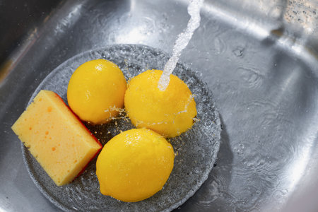 Lemons in a sink under running water.の写真素材