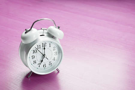 White clock alarm clock showing seven o'clock on purple background with copy space.