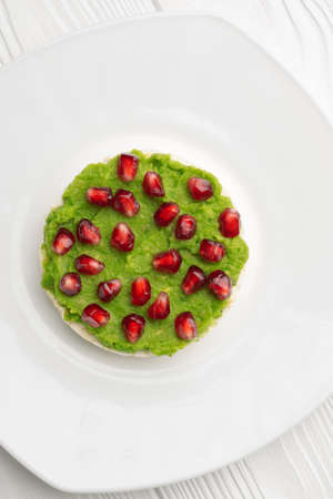 Close up rice cakes with avocado mash and pomegranate seeds in white plate vertical shot.