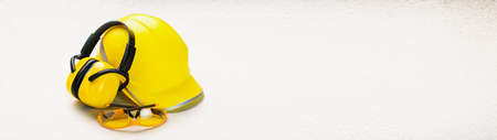 Yellow helmet and earphones with goggles with copy space banner: personal health and safety...