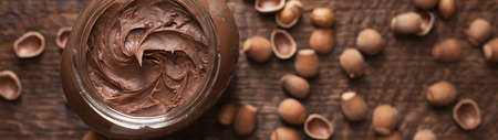 Chocolate-nut paste spread in a glass jar on a wooden background banner.の写真素材