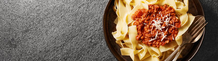 A plate of fresh pappardelle pasta with BOLOGNESE SAUCE on a gray stone background.One object. Web banner with copy space. top view.の写真素材