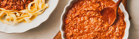 A white bowl of fresh bolognese sauce and a plate of fresh tagliatelle pasta with bolognese sauce. Web banner with copy space. top view.の写真素材