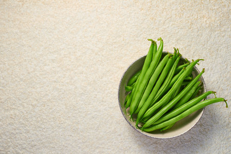A bowl with pods of raw asparagus beans and a knife on a light marble background with copy space....