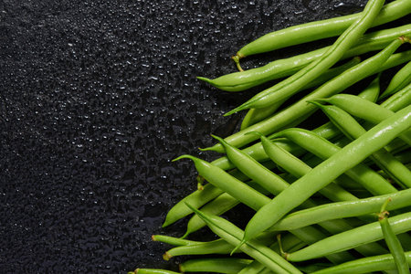 A group of green pods of raw, uncooked, asparagus beans on a black stone background. top view....