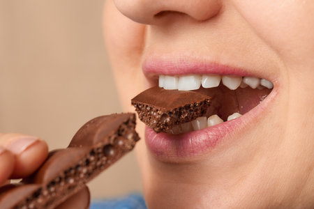 Close up of the mouth of a Caucasian woman biting off a piece of porous chocolate. Three-quarter front view. Low angle view.の写真素材