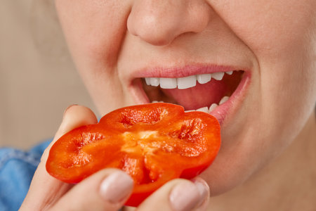 Close-up of a Caucasian woman holding a slice of sweet pepper in her hands and bringing it to her mouth. Front view from low angle.の写真素材