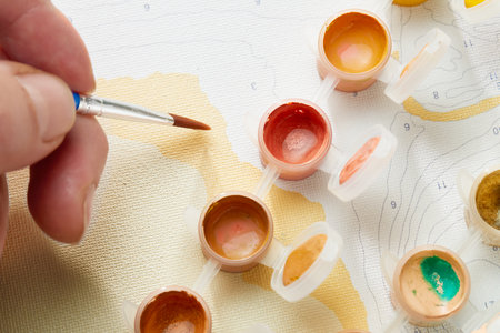 Hand with brush painting by numbers and jars of acrylic paint. Top view.の写真素材