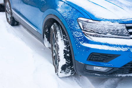 Three-quarter view of the front of a blue modern car standing on a snow-covered road.の写真素材