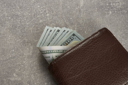 Leather brown wallet with one hundred dollar bills. On a gray background. Close-up. Top view.の写真素材