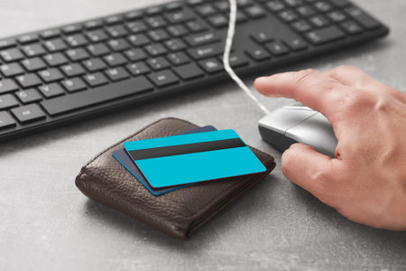 Bank cards and the hand of a white Caucasian man with a computer mouse and keyboard on the table. No face. Indoors.の写真素材