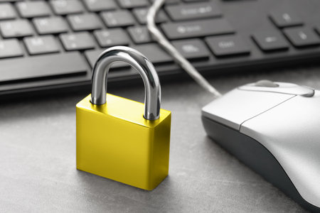 Locked golden padlock and computer mouse with keyboard on the table. Cybersecurity concept.の写真素材