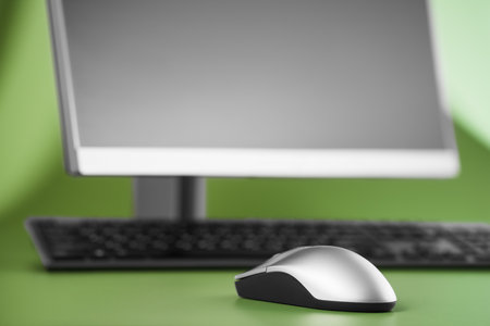 Modern computer monitor with keyboard and mouse on a green background. Selective focus on mouse