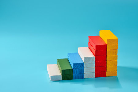 Stacked colorful wooden blocks form a staircase pattern against a vibrant blue background, providing an engaging visual for children's educational playtime and creativity development.の写真素材