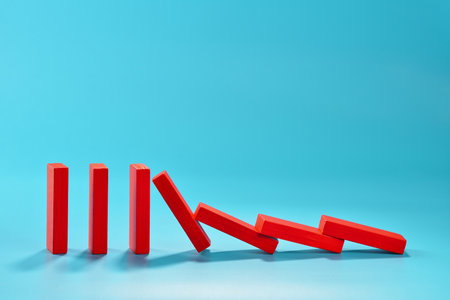 A series of red rectangular dominoes stands upright, with the first few tipping over and creating a chain reaction. copy spaceの写真素材