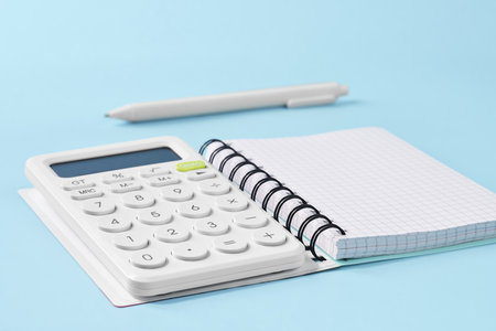 A calculator and a blank notebook sit on a blue surface, ready for study or task organization.の写真素材
