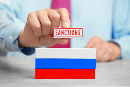 A man holds a wooden block with the text "Sanctions" and the Russian flag.の写真素材