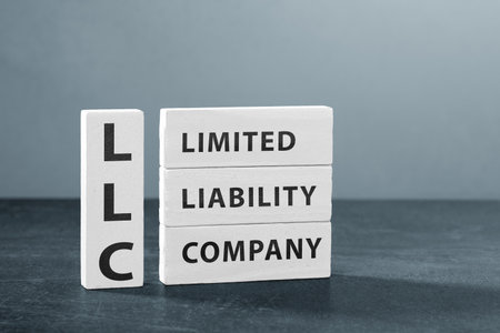 Wooden blocks with the words "Limited Liability Company" placed on a clean gray background, symbolizing the process of business registration and small enterprise formation. This minimalistic and professional composition represents entrepreneurship, startup growth, and the legal foundation of a new company. Perfect for illustrating topics like business structure, corporate management, and brand establishment.の写真素材
