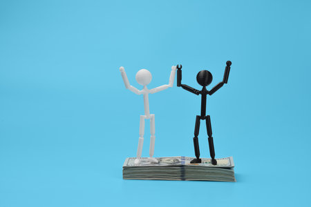 Two figures raise hands on dollar stack, symbolizing financial victory and success.の写真素材