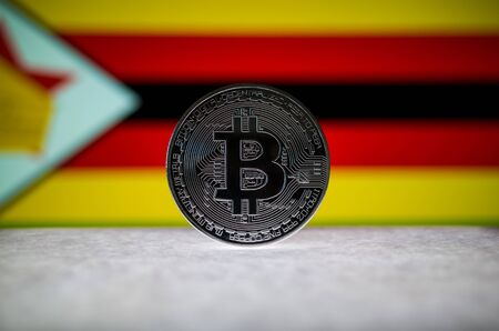 Physical silver version of Bitcoin BTC and Zimbabwe Flag on the background. Conceptual image for investors in cryptocurrency and Blockchain Technology.の写真素材